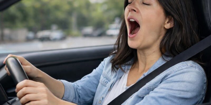 Donna alla guida che sbadiglia per sonnolenza causata da apnea notturna